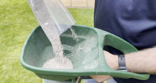 pouring fertiliser into a handheld fertiliser spreader
